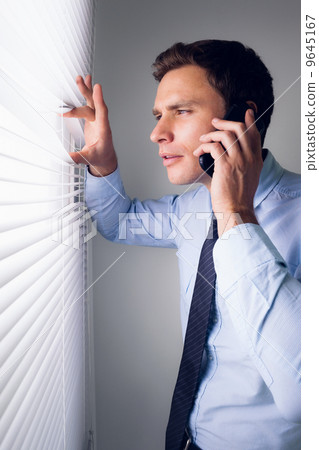 Businessman peeking through blinds while on call in office 9645167