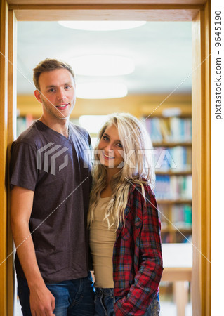 Smiling couple against blurred bookshelf in library Smiling couple against blurred bookshelf in library 9645190
