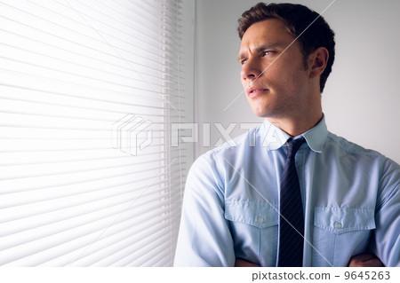 Businessman peeking through blinds in office 9645263