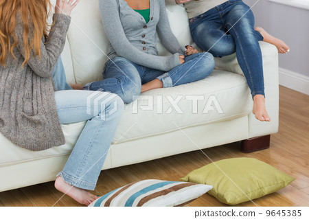 Friends sitting on sofa with cushion on floor at home Friends sitting on sofa with cushion on floor at home 9645385