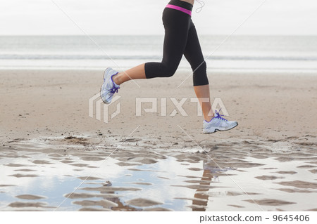 Low section of healthy woman jogging on beach 9645406