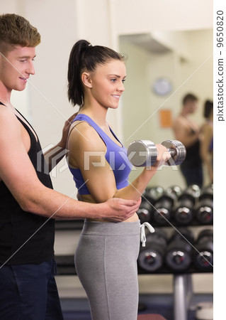 Male trainer helping young woman with the dumbbells in gym 9650820