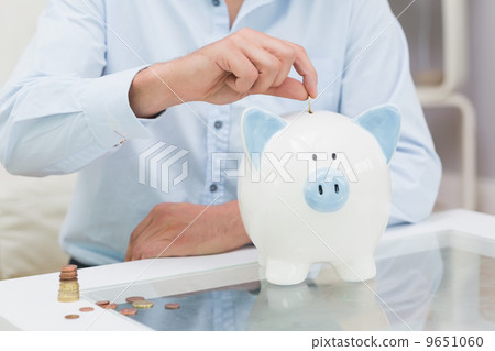 Mid section of a man putting some coins into a piggy bank 9651060