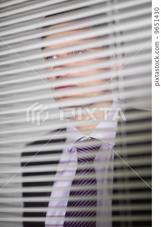 Businessman peeking through blinds in office Businessman peeking through blinds in office 9651430