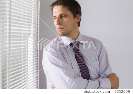 Serious businessman peeking through blinds in office 9652099