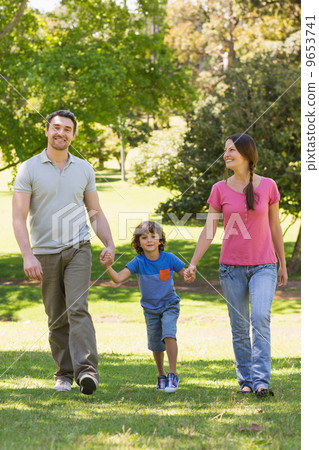Family of three holding hands and walking at park 9653741