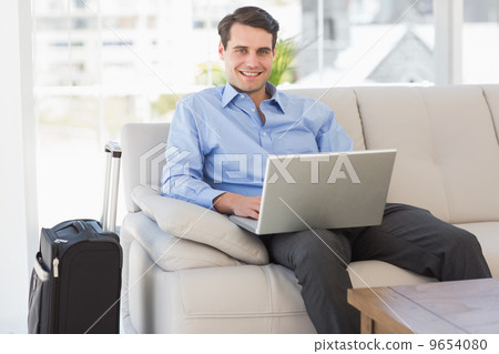 Travelling businessman using laptop sitting on the couch smiling Travelling businessman using laptop sitting on the couch smiling 9654080