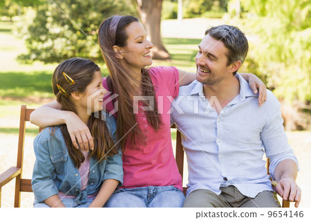 Smiling couple with daughter sitting on park bench 9654146