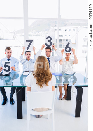 Group of panel judges holding score signs in front of woman 9654159