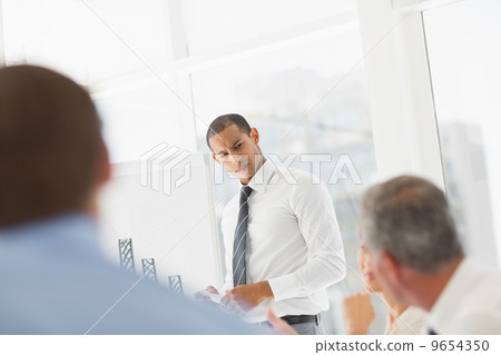 Serious businessman presenting bar chart to co workers 9654350
