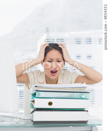 Angry businesswoman shouting with stack of folders at desk 9654351