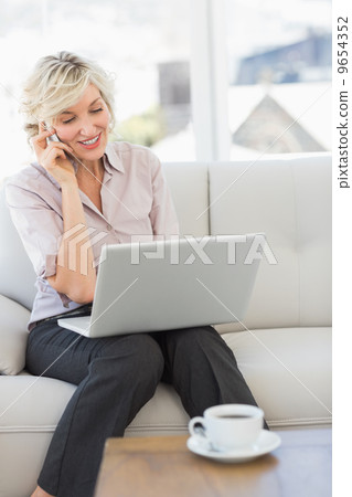 Businesswoman using mobile phone and laptop at home Businesswoman using mobile phone and laptop at home 9654352