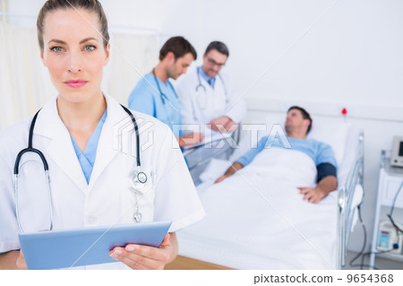 Doctor using digital tablet with colleagues and patient behind 9654368