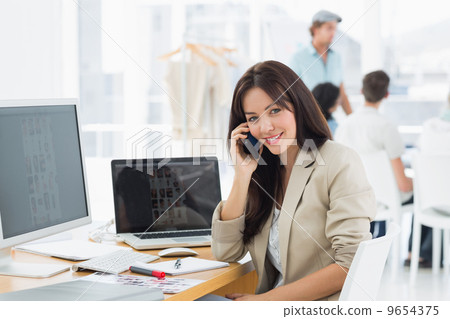 Woman on call at desk with colleagues behind in office 9654375