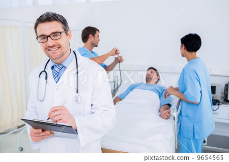 Doctor writing reports with patient and surgeons in background Doctor writing reports with patient and surgeons in background 9654565