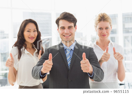 Smiling businessman giving thumbs up with his team 9655115