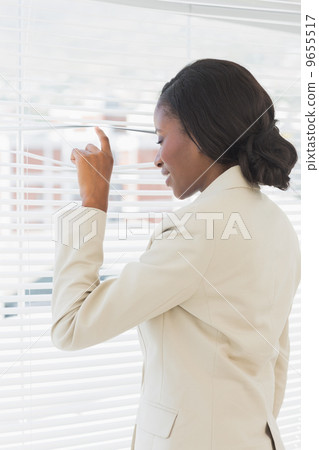 Businesswoman peeking through blinds in office Businesswoman peeking through blinds in office 9655517
