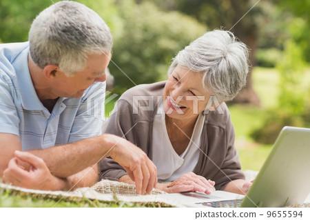 Smiling senior couple using laptop at park Smiling senior couple using laptop at park 9655594