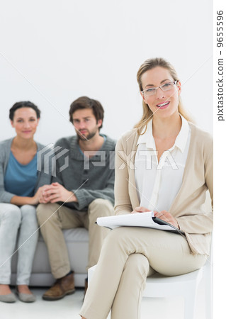Female financial adviser with young couple in background Female financial adviser with young couple in background 9655596