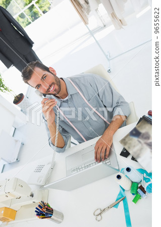 Fashion designer using laptop and phone in studio Fashion designer using laptop and phone in studio 9655622