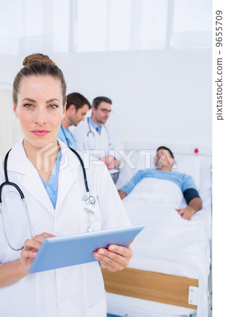 Doctor using digital tablet with colleagues and patient behind 9655709