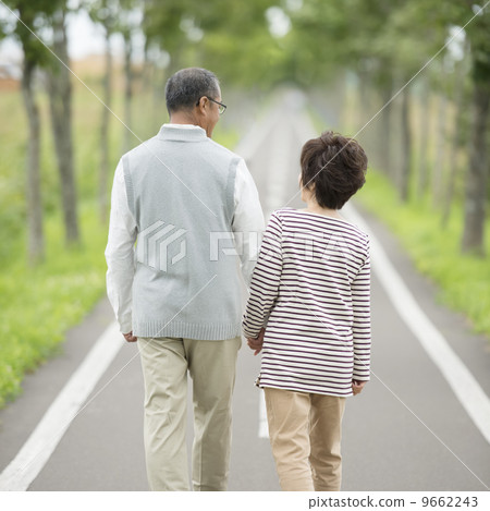 Rear of senior couple walking along one road connecting hands 9662243