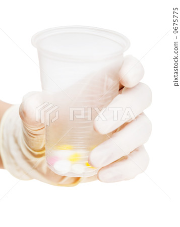 gloved hand holding plastic cup with pills 9675775