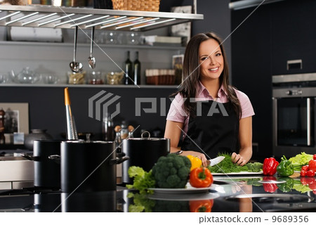 Cheerful young woman in apron on modern kitchen cutting vegetables Cheerful young woman in apron on modern kitchen cutting vegetables 9689356