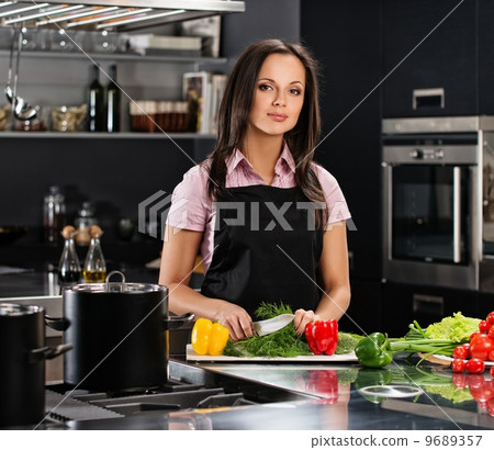 Cheerful young woman in apron on modern kitchen cutting vegetables Cheerful young woman in apron on modern kitchen cutting vegetables 9689357