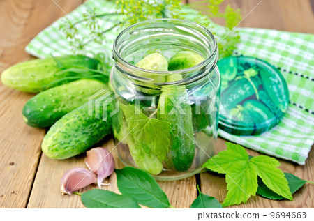 Cucumbers in jar with leaves and napkin on the board Cucumbers in jar with leaves and napkin on the board 9694663