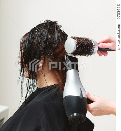 In hairdressing salon. Hairstylist with dryer drying hair of woman client. 9705458