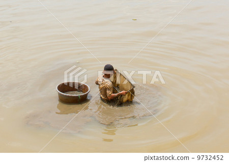 A vietnamese fisherman is searching for shells in the water A vietnamese fisherman is searching for shells in the water 9732452