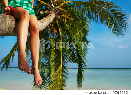 Woman sitting on a palm tree at tropical beach 9765862