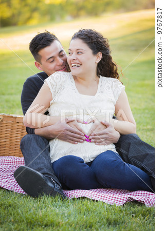 Pregnant Hispanic Couple Making Heart Shape with Hands on Belly 9767817