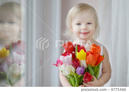 Adorable toddler girl with tulips by the window Adorable toddler girl with tulips by the window 9775480