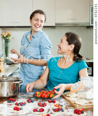 Two smiling women making perogies with berries Two smiling women making perogies with berries 9782191
