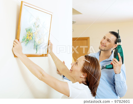 middle-aged man and woman hanging art picture in frame middle-aged man and woman hanging art picture in frame 9782601