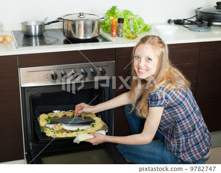 Positive woman cooking fish in oven at kitchen Positive woman cooking fish in oven at kitchen 9782747
