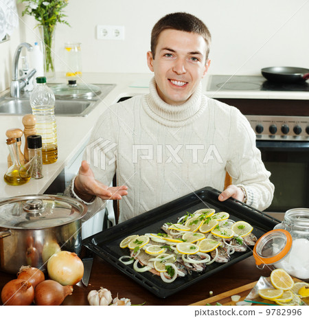 Handsome man with raw fish on roasting pan Handsome man with raw fish on roasting pan 9782996