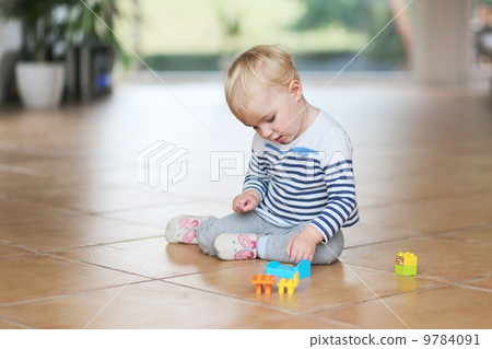 Cute little baby girl play with plastic bricks sitting indoors on a tiles floor Cute little baby girl play with plastic bricks sitting indoors on a tiles floor 9784091