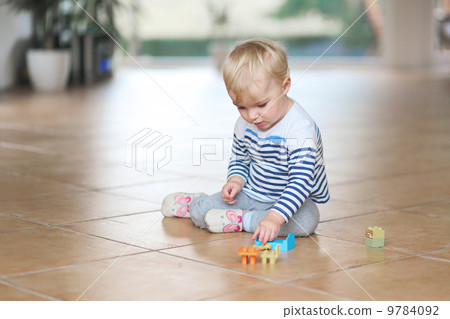 Cute little baby girl play with plastic bricks sitting indoors on a tiles floor Cute little baby girl play with plastic bricks sitting indoors on a tiles floor 9784092