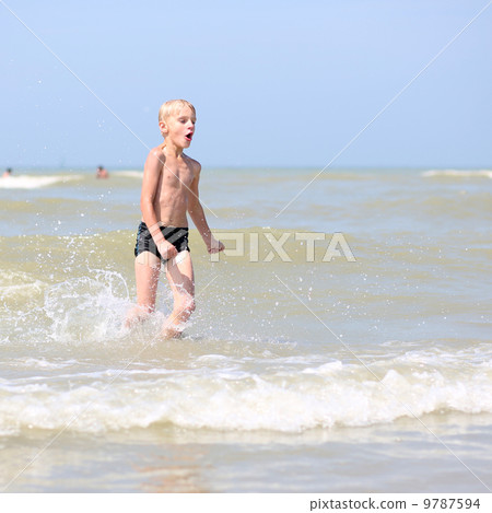 Happy teenager boy plays on the beach enjoying sun and the sea splashing the water Happy teenager boy plays on the beach enjoying sun and the sea splashing the water 9787594