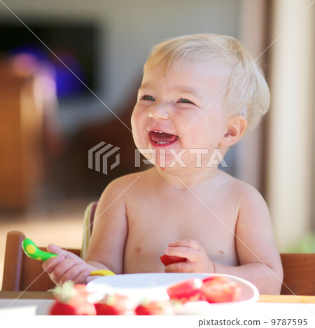 Funny happy healthy toddler sitting in high feeding chair eating cherry tomato Funny happy healthy toddler sitting in high feeding chair eating cherry tomato 9787595