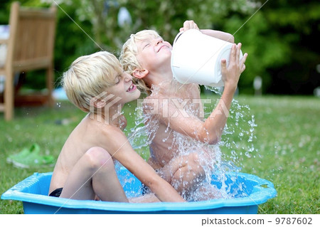 Kids playing with water in little plastic bath outdoors in the garden at the backyard of the house 9787602
