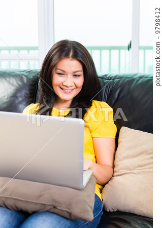 Asian woman using laptop on couch 9798412