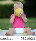 Adorable little girl is sitting on a carpet in a park and biting on a half of melon 9820928