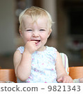 Funny happy healthy toddler sitting in high feeding chair biting on cherry tomato 9821343