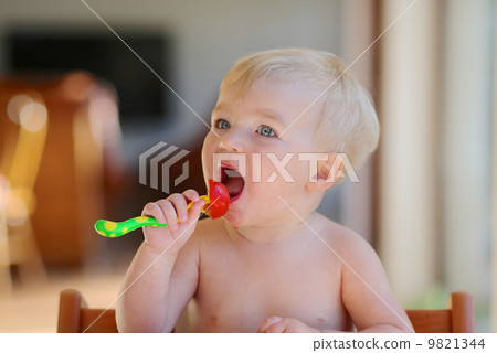 Funny happy healthy toddler sitting in high feeding chair eating cherry tomato 9821344