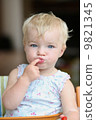 Funny happy healthy toddler sitting in high feeding chair biting on cherry tomato 9821345