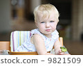 Cute baby girl sitting in a high feeding chair biting on delicious freshly cooked broccoli  9821509
